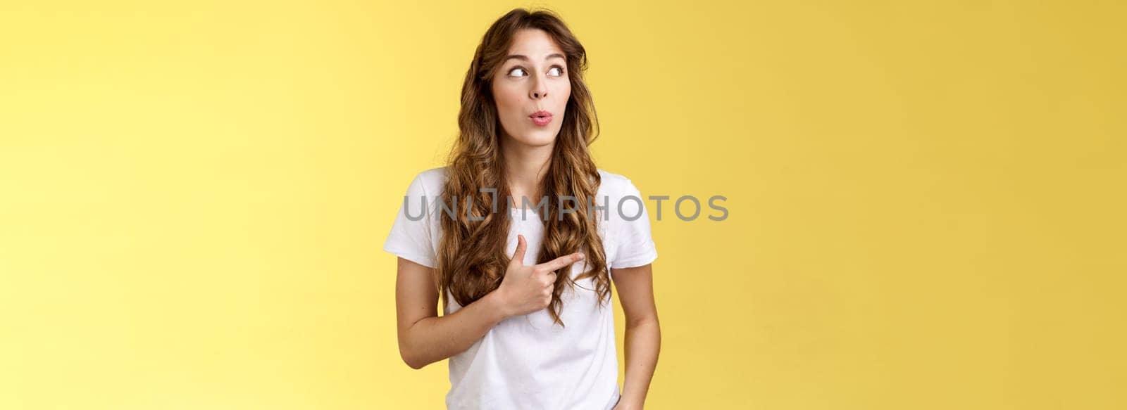 Hmm interesting wow. Curious silly cute pretty woman long curly hairstyle folding lips admiration tempting try out new menu look pointing upper left corner fascinated intrigued yellow background.