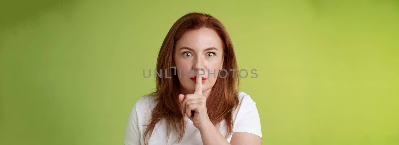 Hush not say that. Worried shocked redhead middle-aged wife demand keep mouth shut shushing ask silence stop spread false rumours stare camera hold index finger pressed lips taboo gesture.