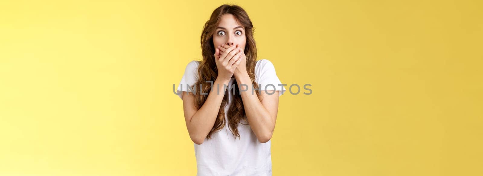 Shocked ambushed speechless cute girl hear impressive rumor shut mouth hold hands lips stare camera astonished eavesdrop juicy stunning conversation stand yellow background. Copy space