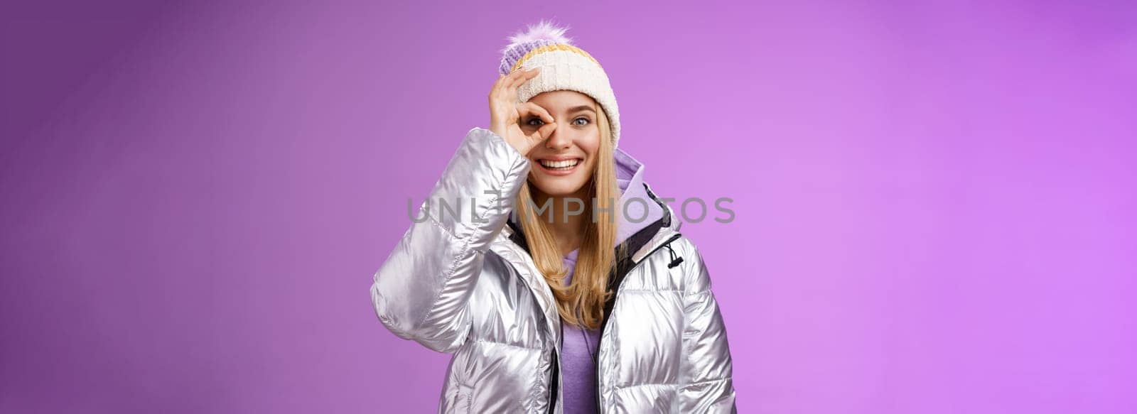 Stylish carefree european female student enjoying vacation trip snowy country wearing warm trendy silver jacket knitted hat show okay ok awesome gesture smiling having fun recommend resort by Benzoix