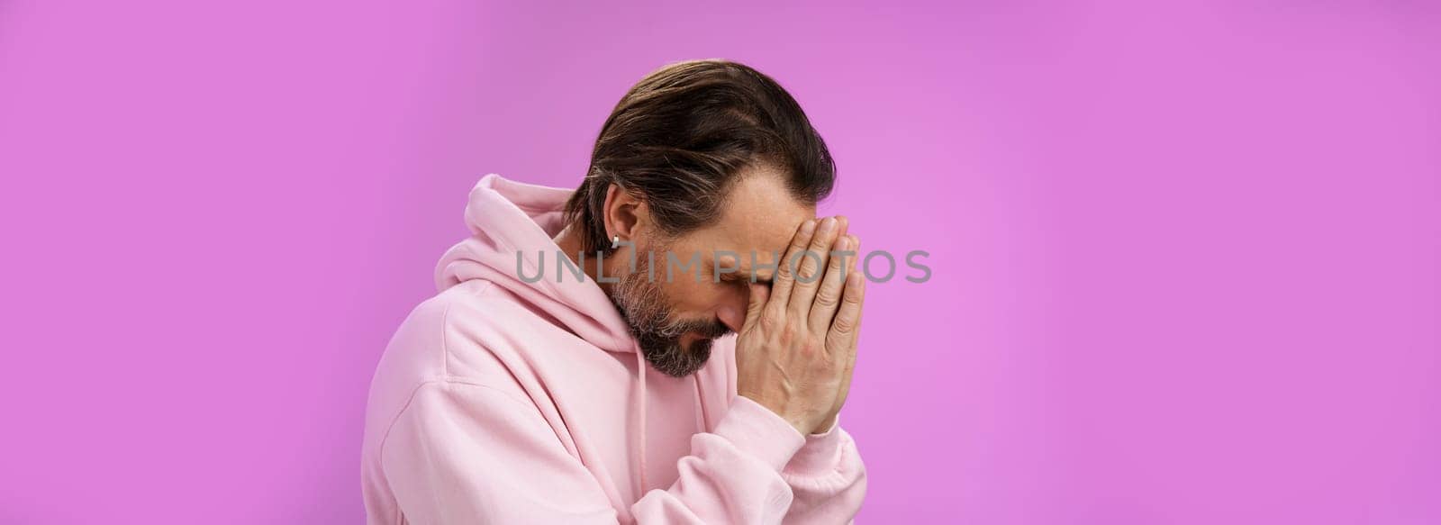 Concerned upset man supplicating asking god mercy help praying bow head close eyes hold hands pray hopefully waiting miracle worried wife health, standing sadness purple background by Benzoix