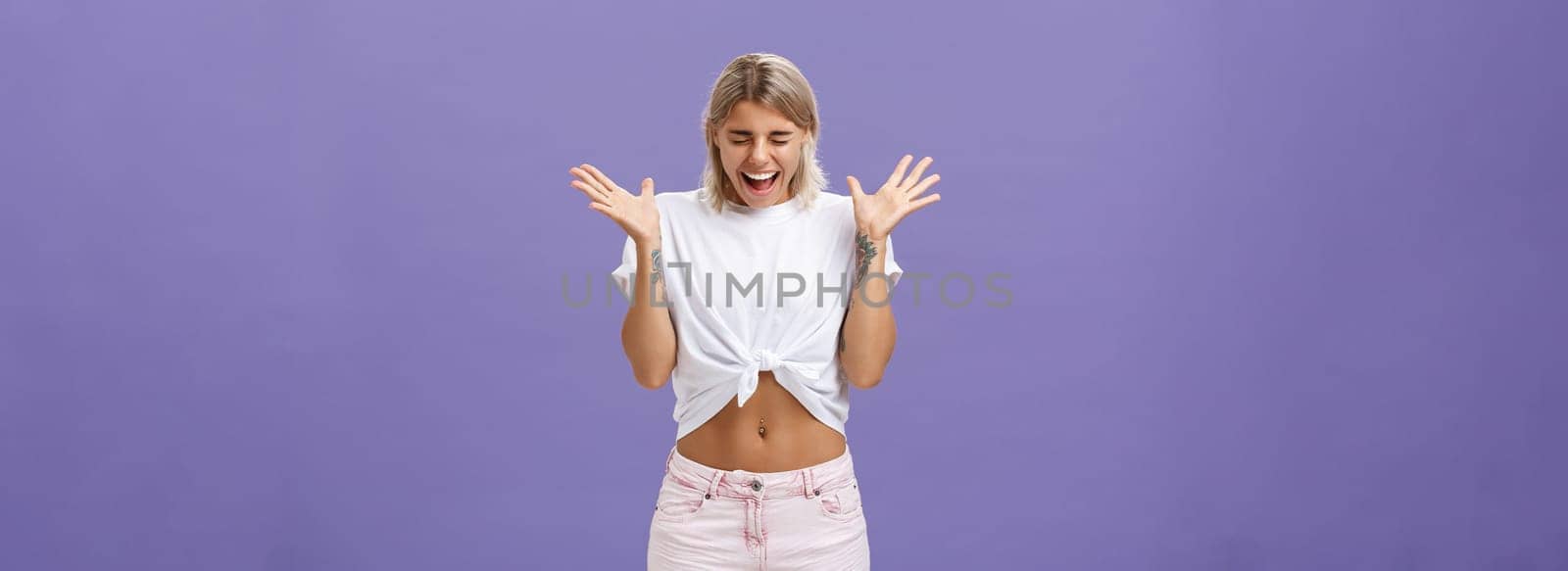 Studio shot of woman having mental breakdown screaming out loud shaking raised palms closing eyes and bending head down feeling scared and yelling from fear over purple background. Emotions concept