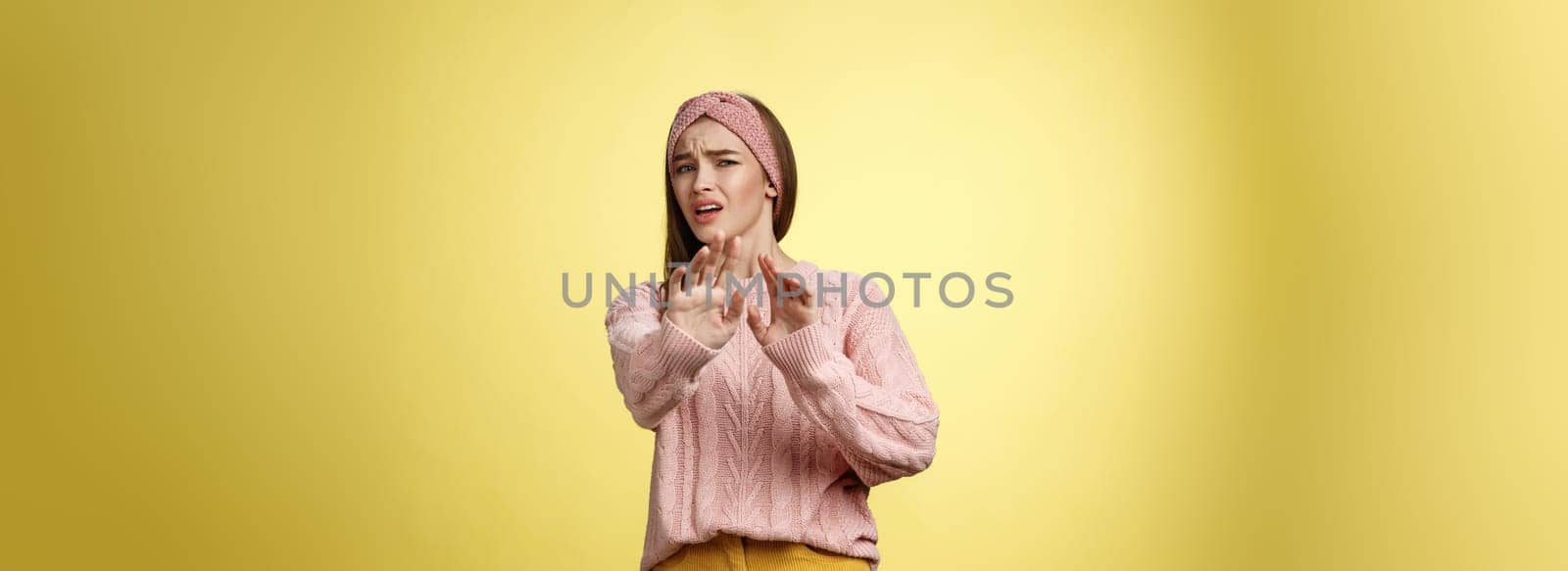 Omg no. Cute young european schoolgirl step back stooping grimacing disgusted and displeased turning away reluctant expressing aversion extending palm in rejection, refusal gesture over yellow wall by Benzoix