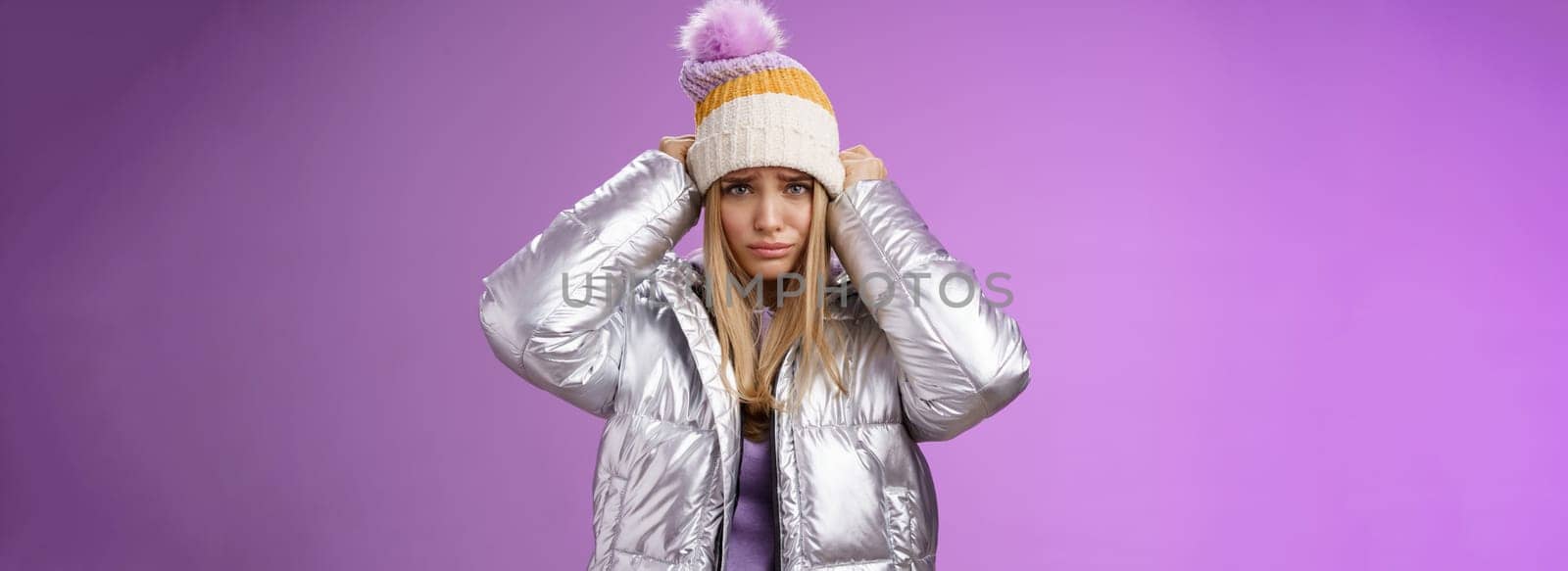 Upset gloomy complaining blond girlfriend whining standing upset disappointed sulking offended pulling hat forehead look offended unhappy wearing stylish glittering jacket unwilling go outside cold.