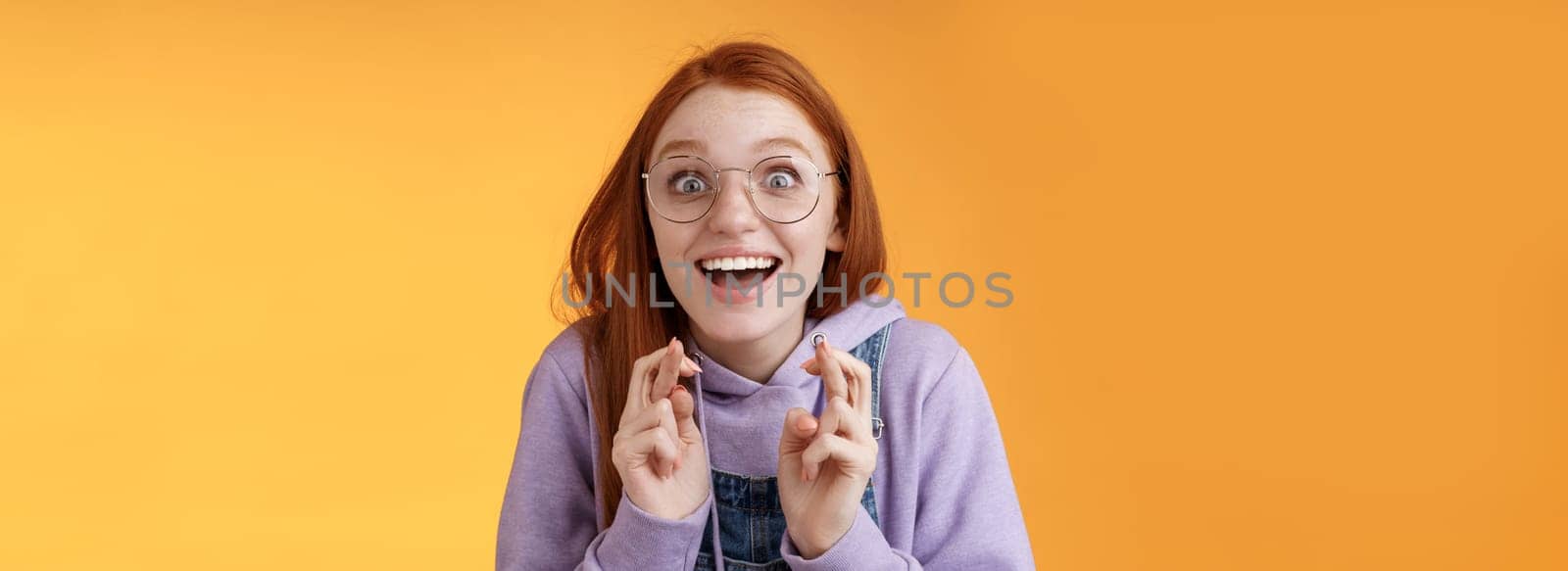 Surprised girl dream came true celebrating standing amused excited cross fingers good luck wish fulfilled smiling emotive thrilled finally win receive good news optimistic hopeful orange background by Benzoix