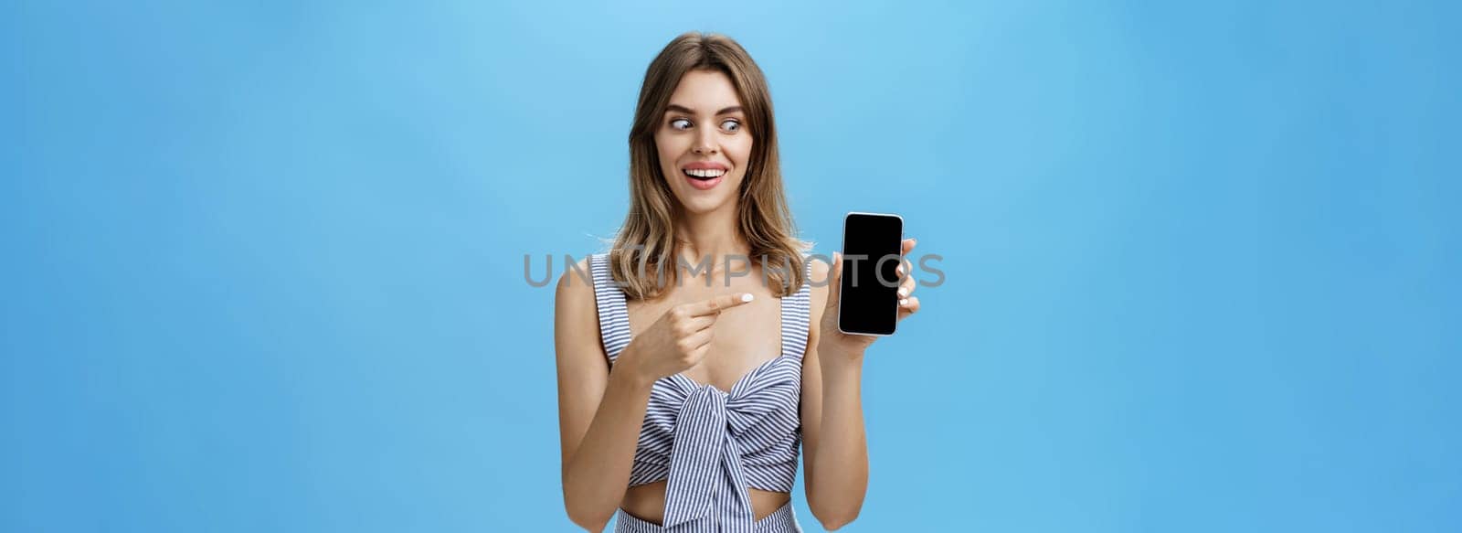 Portrait of charismatic astonished and happy woman with cute gapped teeth smiling axcited and surprised holding awesome smartphone pointing at device screen and looking at gadget amazed and delighted. Lifestyle.