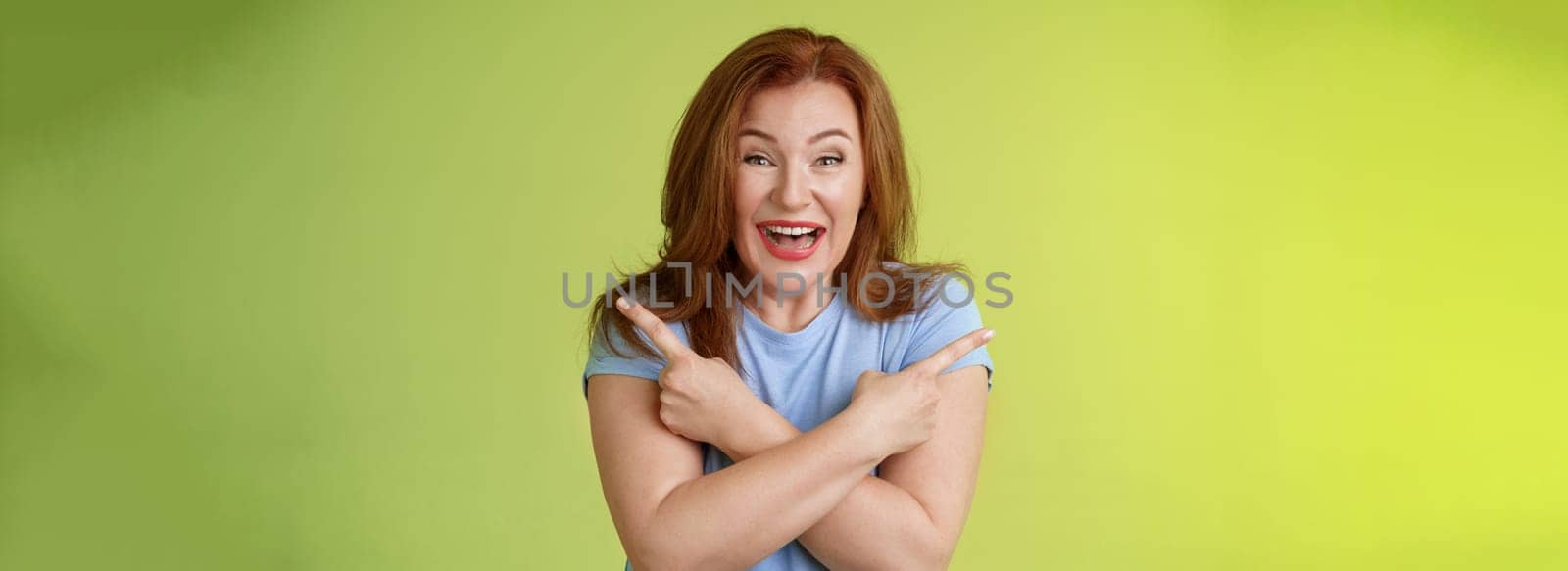 Lifestyle Concept - Happy carefree entushiastic redhead funny mature female. having fun positive attitude cross arms body pointing sideways show left right products laughing happily like both choices green background.