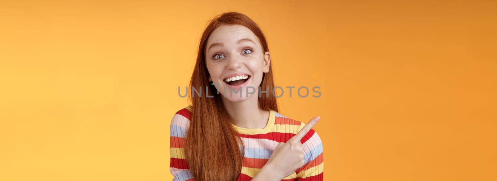 Amused carefree thrilled emotional redhead female fan adore talking favorite movie pointing upper left corner fascinated smiling broadly happy delighted attend incredible party, orange background. Lifestyle.