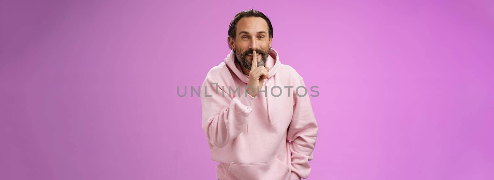Lips sealed secret. Portrait alluring cheeky stylish adult bearded guy in pink hoodie asking keep quiet show shush shh gesture index finger pressed mouth smiling devious smug face, have idea by Benzoix
