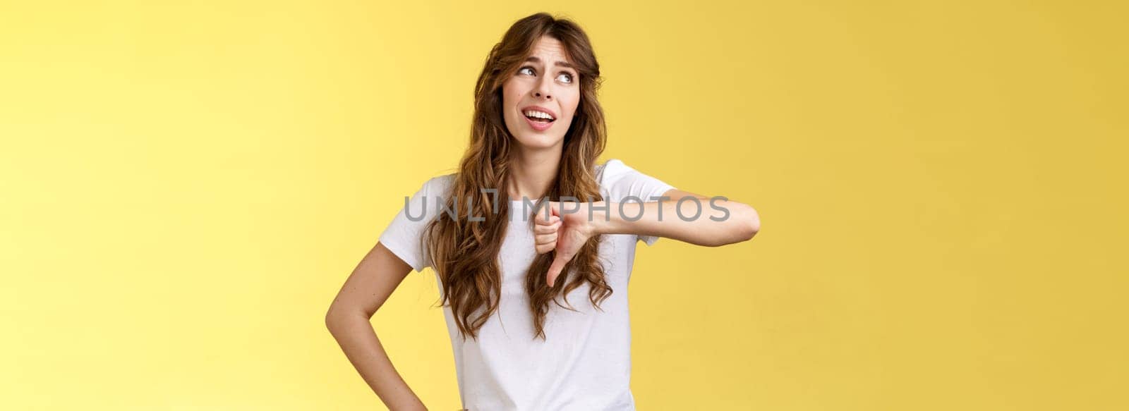 Blah blah boring. Unimpressed apathetic snobbish attractive curly-haired girl look away express scorn disdain show thumb down frowning sharing negative judgement bad opinion yellow background by Benzoix
