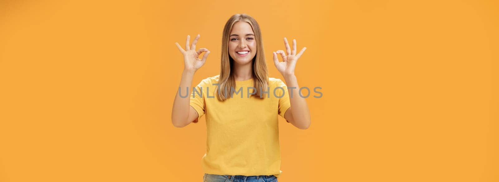 Optimistic charming woman with fair hair and no make-up in yellow t-shirt showing okay or approval gesture assuring everything ok and nothing to worry she can handle project alone, smiling confident. Emotions and body language concept