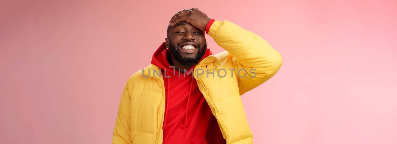 Charming cute black bearded 25s guy forget something stupid silly smiling friendly punch forehead grinning feel awkward say sorry standing pink background joyfully relaxed by Benzoix