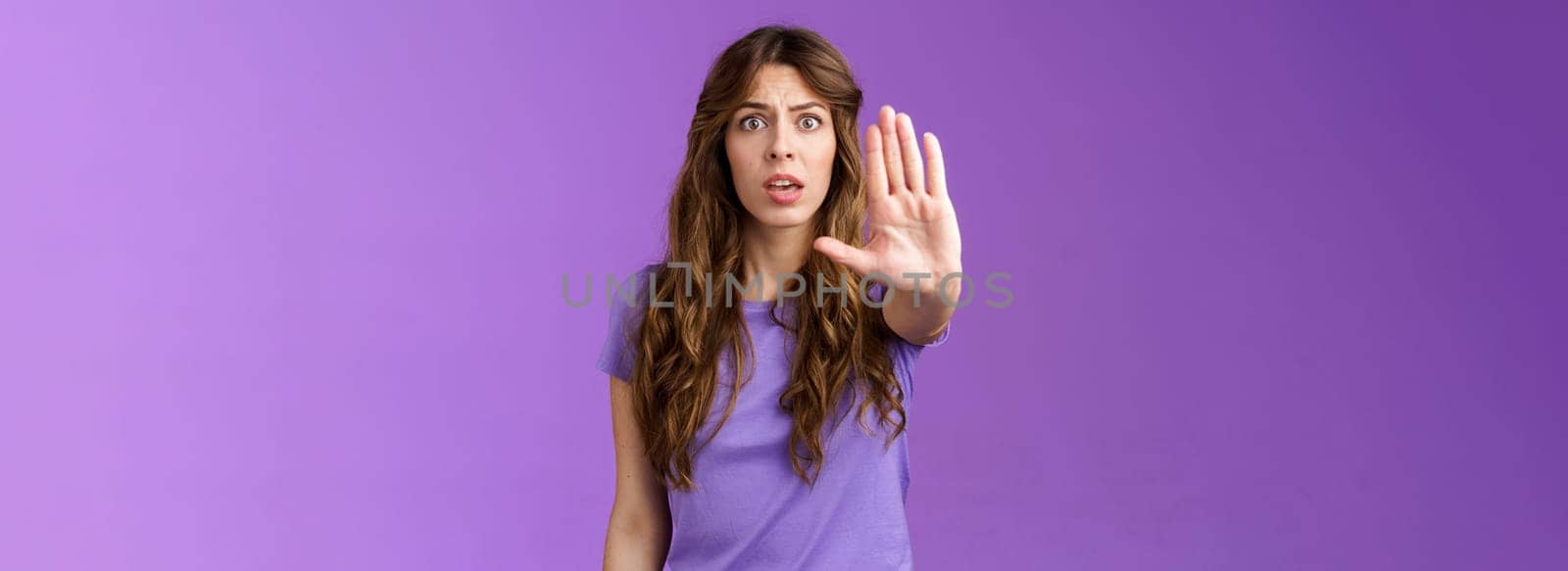 Worried shocked curly-haired woman gasping stare camera anxiously pull hand stop sign begging end prohibiting friend drive after drinking stand purple background forbid warn you purple background by Benzoix