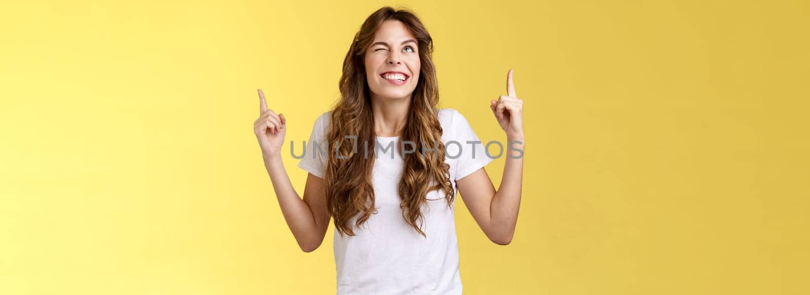 Cheeky confident positive attractive female optimistic joyful vibe smiling toothy wink grinning look up sassy pointing top making deal god hinting making cunning mood stand yellow background. Lifestyle.
