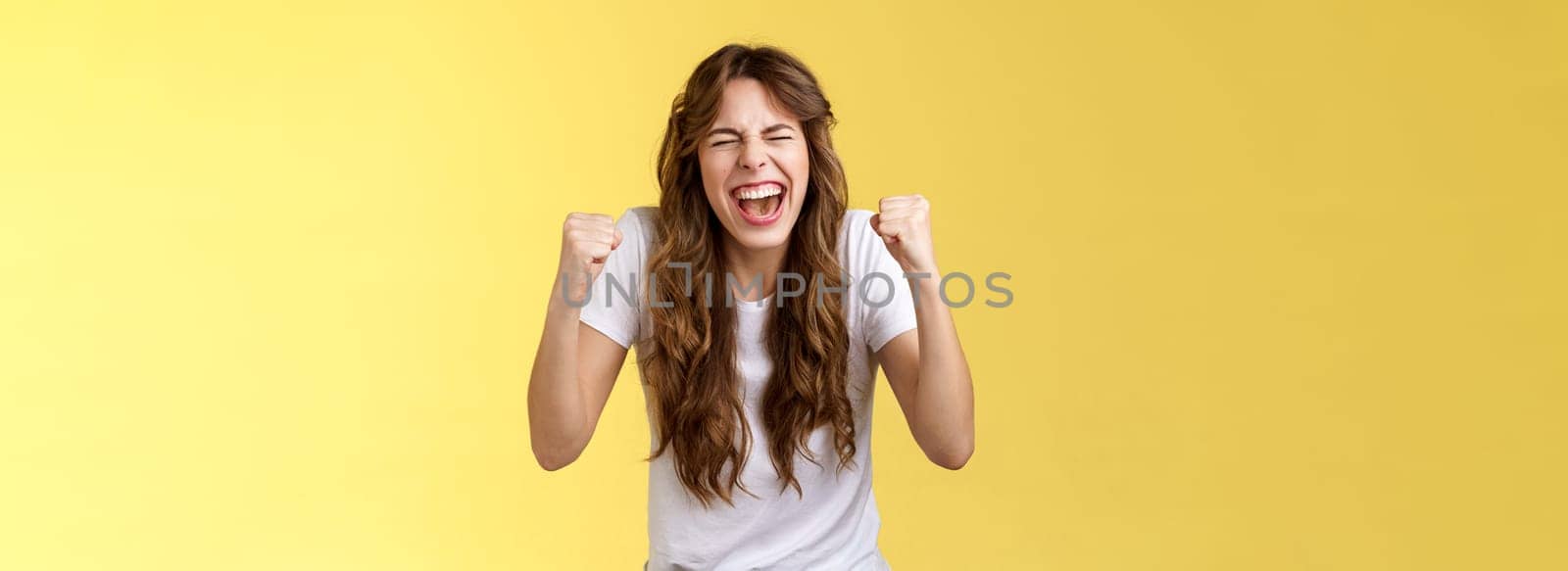 Cheerful excited happy enthusiastic girl yelling rooting wanna win badly fist pump celebratory satisfied awesome success winning triumphing joyfully close eyes shaking clench arms yellow background. Lifestyle.