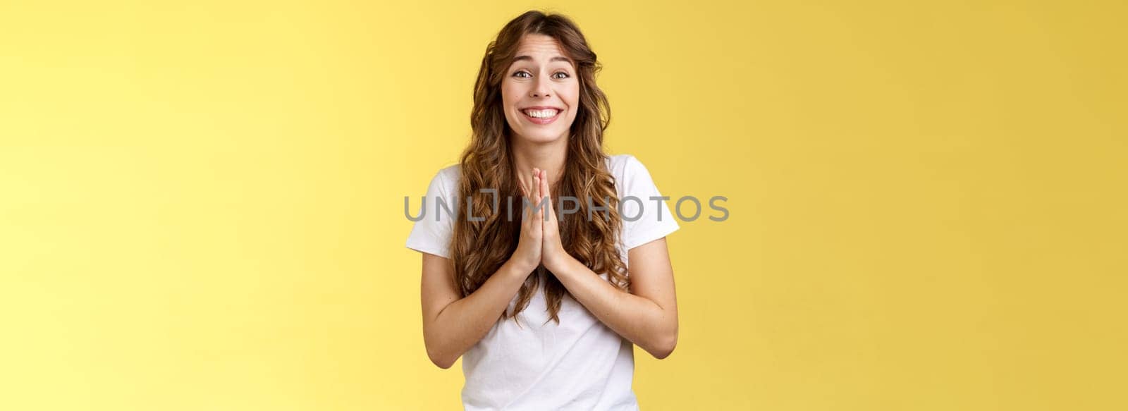 Please one small favor. Cute silly charming young girlfriend asking lend money press palms together praying supplication gesture implore you help hopefully smiling begging yellow background.