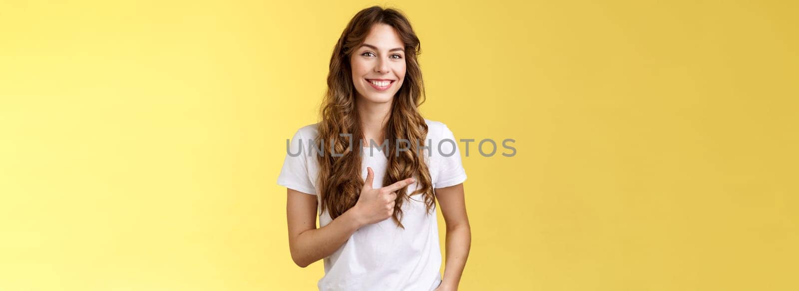 Sassy confident happy charismatic young woman long curly hairstyle hold hand pocket relaxed outgoing expression pointing left index finger inviting local cafe discuss friend favorite places. Lifestyle.