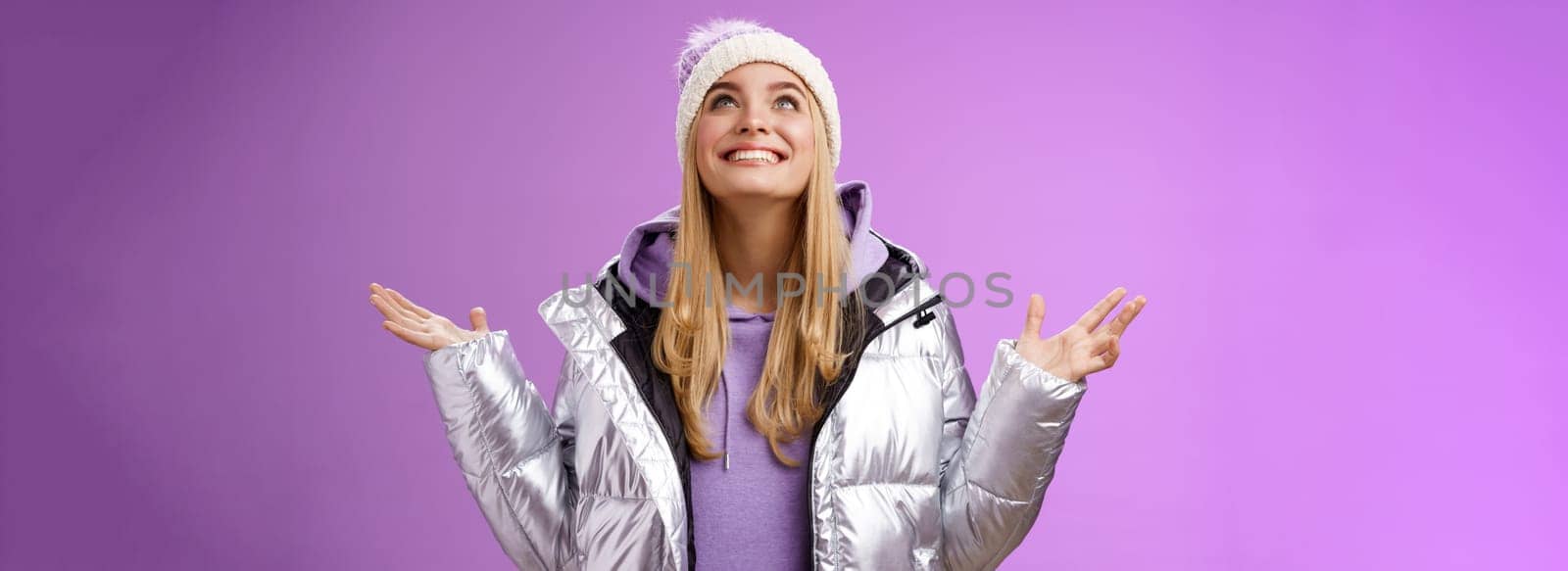 Thankful happy cute attractive blond young 25s woman in winter hat silver trendy jacket raise hands look up grateful god dream come true smiling delighted fulfilled wish, purple background by Benzoix