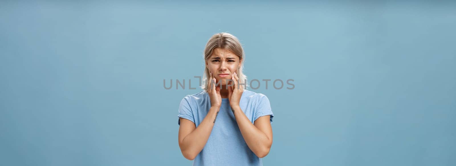Girl feeling pain in teeth after drinking hot coffee. Displeased unhappy troubled young girl with blond hair frowning feeling discomfort in mouth holding hands on cheeks suffering toothache by Benzoix
