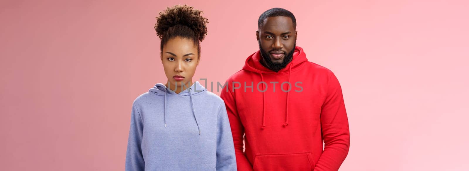 Two cute african american siblings standing together pink background invited family dinner greet new mom boyfriend, sister look displeased serious brother smug have idea prank stepdad.