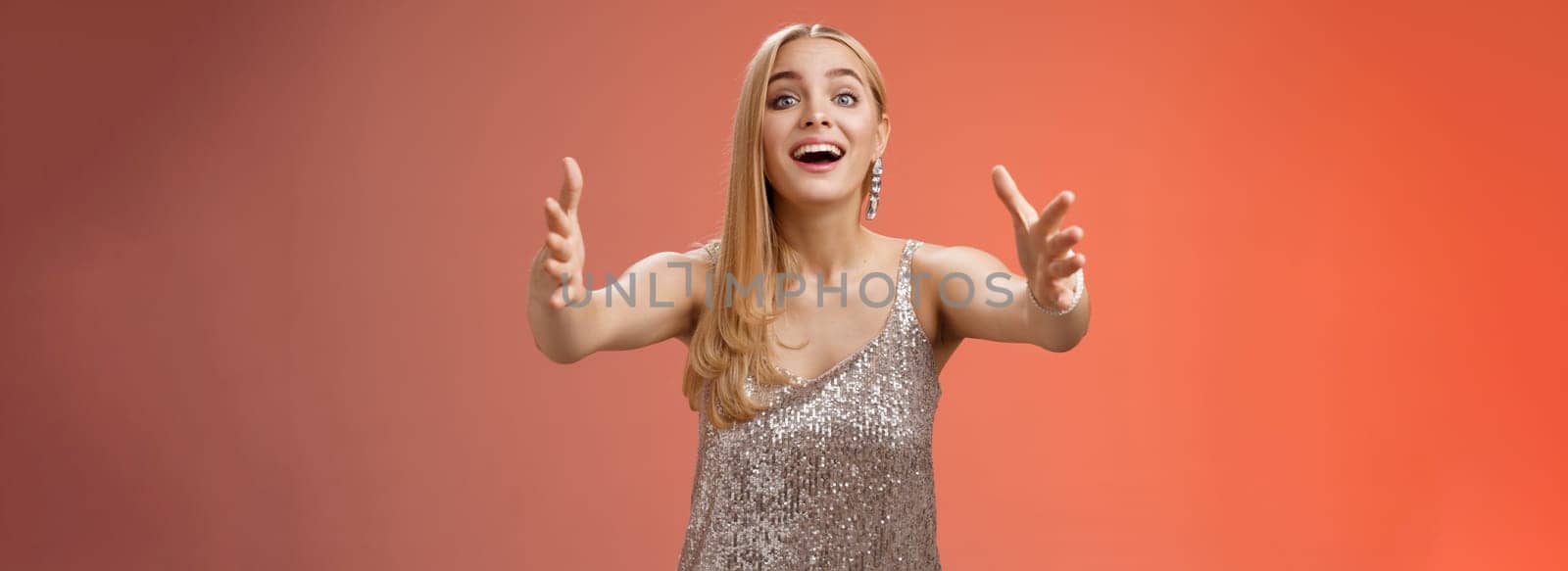 Excited charmign touched hearwarming young blond woman in silver party glamour dress stretch hands towards camera amused wanna hug cuddle hold cute puppy arms, standing red background by Benzoix