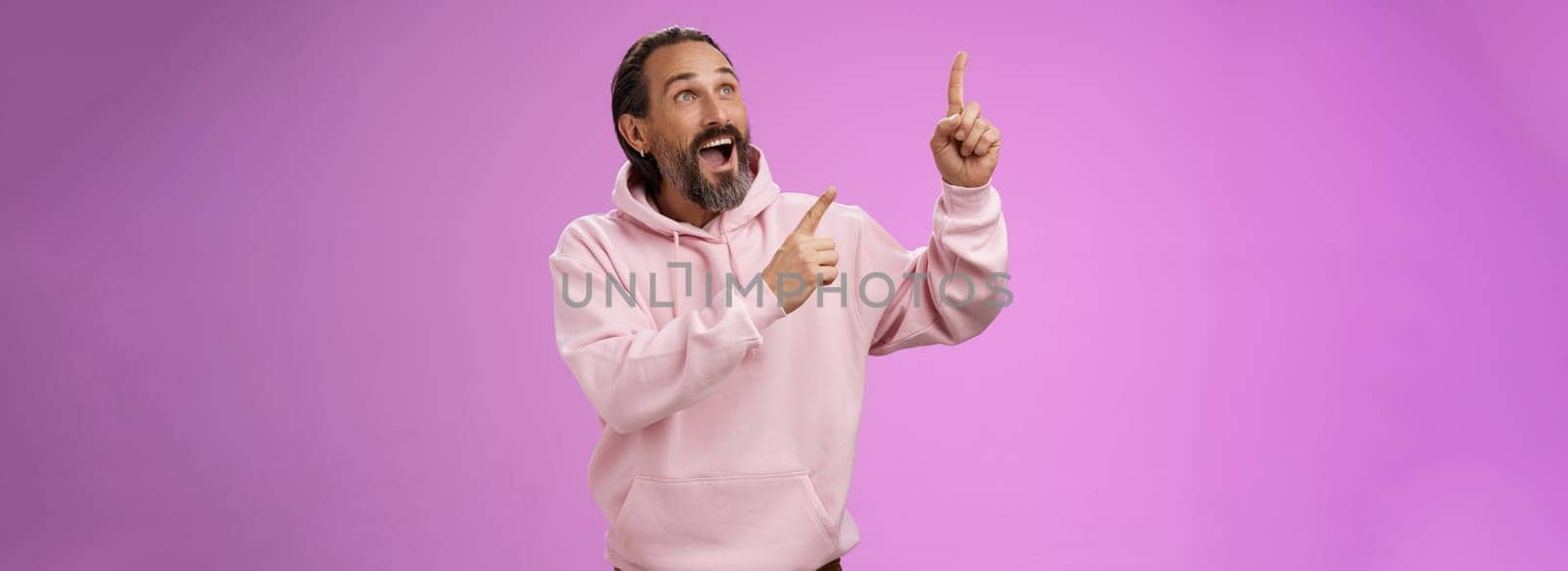 Fashionable good-looking fascinated mature bearded man grey hair look astonished pointing gazing upper left corner see miracle incredible breathtaking magnificanent view, standing purple background.