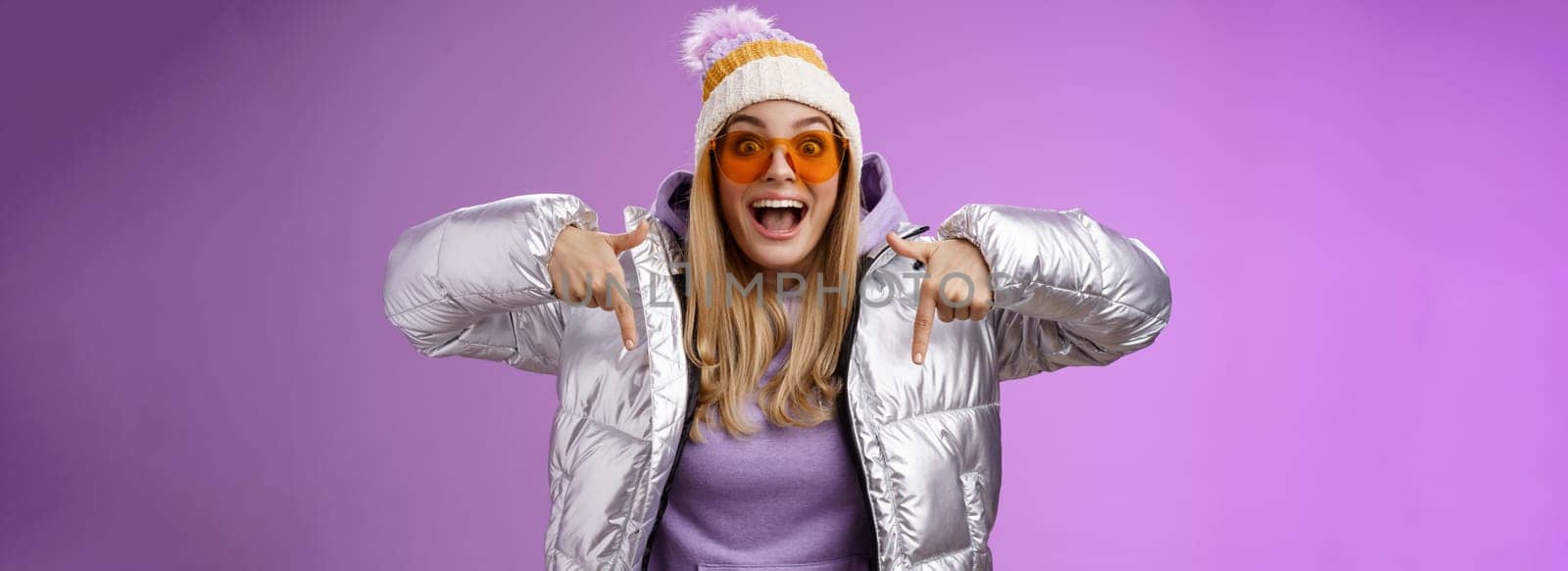 Lifestyle. Excited impressed good-looking blond girl drop jaw amused overwhelmed pointing down index fingers checking out awesome promotion standing surprised thrilled wearing silver winter jacket hat.