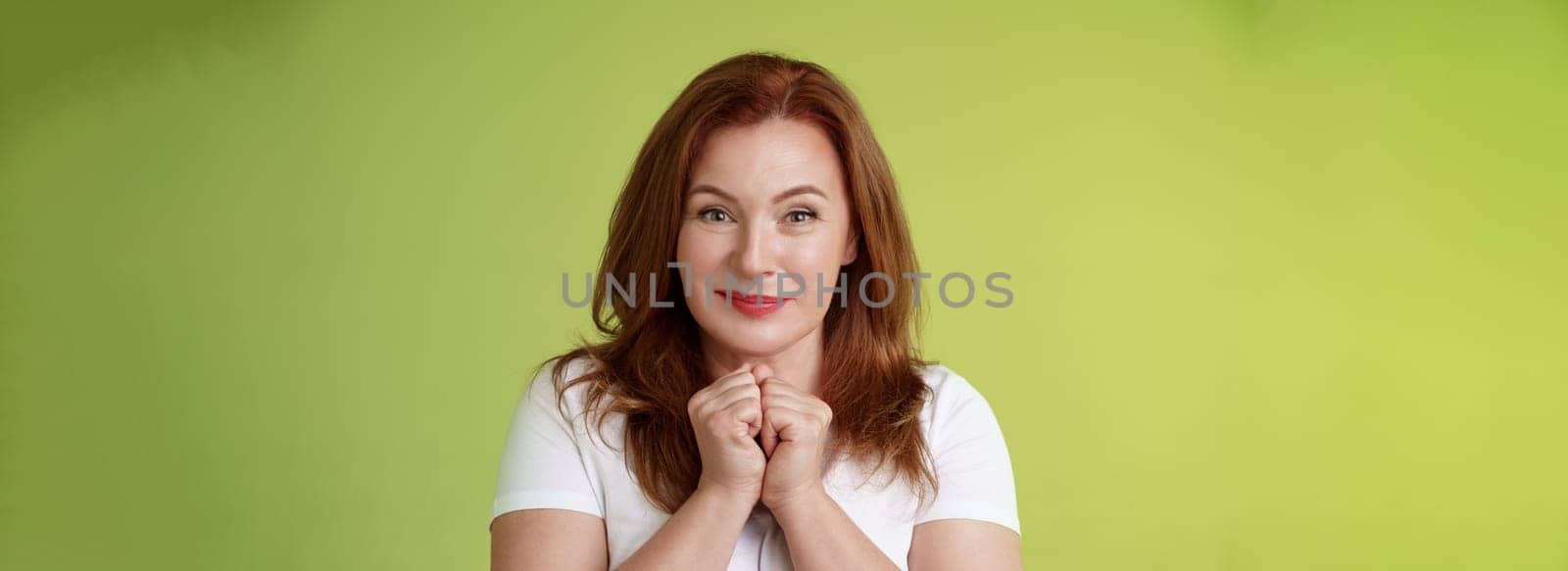 Cheerful lovely pleasant redhead middle-aged female press hands together delight kind happy gaze smiling joyfully touched grateful receive heartwarming gift look admiration happiness.