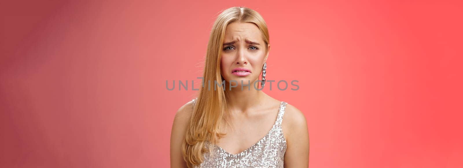 Disappointed complaining cute blond woman in silver stylish dress grimacing frowning upset have bad day pouting pity standing displeased unhappy heartbroken everything bad, red background.