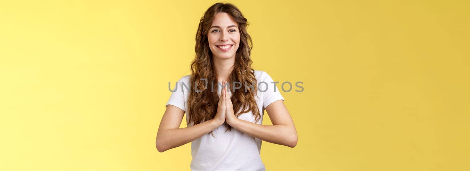 Friendly happy relaxed good-looking woman say namaste smiling broadly relieved feel okay grinning positive vibe press palms together supplication gesture asking offer hopeful yellow background. Lifestyle.