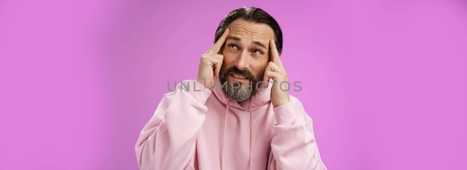 Worried intense disturbed mature male writer cannot create idea standing pressured touch forehead frowning look up problem concentrate not focused, standing purple background upset distracted.