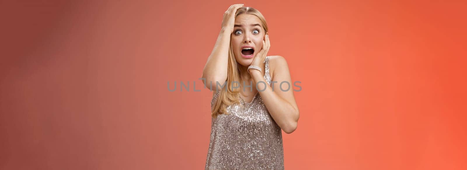 Shocked terrified blond woman horrified see crime screaming pop eyes shouting hold hands head afraid trembling fear standing frightened drop jaw gasping face terrible accident, red background by Benzoix