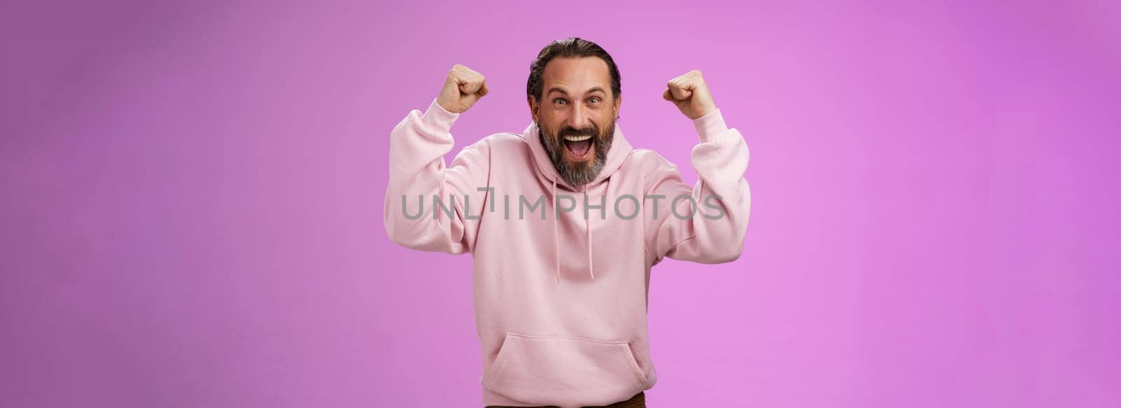 Excited cheering devoted male bearded grey hair yelling supportive words win lottery place good lucky bet standing pleased triumphing say yes raising fists victory success gesture, purple wall.