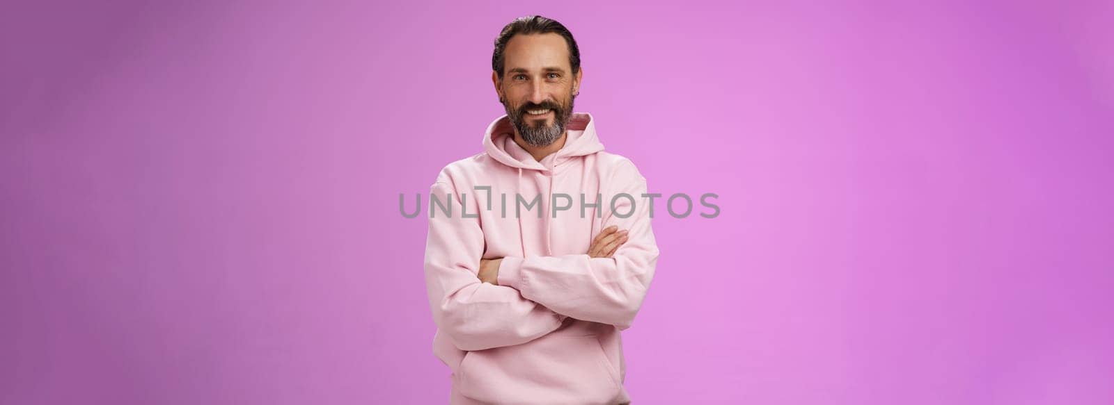 Portrait cool bearded mature grandad trying stay stylish urban trends wear pink hoodie cross arms chest casual pose smiling happily talking have conversation, posing purple background.