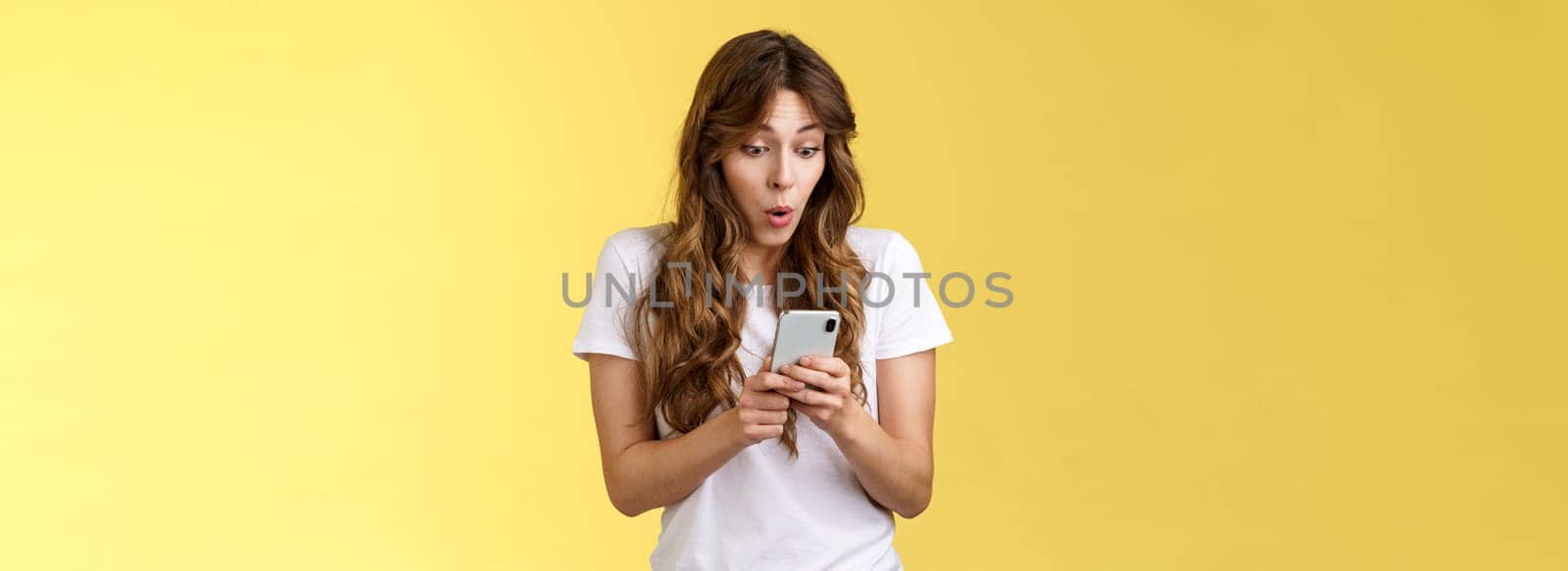 Shocked amazed european girl female blogger become famous online gasping astonished stare camera surprised impressed reading rumors internet social media stand yellow background. Technology concept