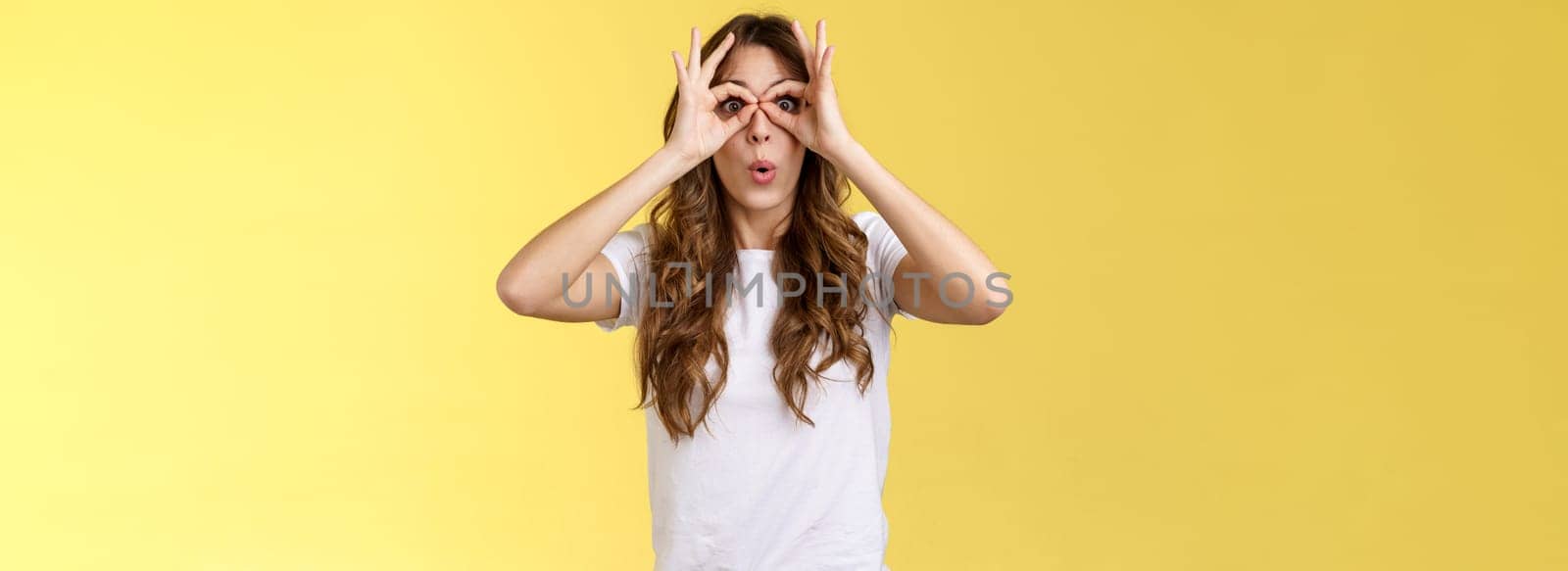 Wow so cool. Girl obersve interesting awesome event show okay perfection gesture look through ring hands folding lips amused wondered glance camera fascinated admiration interested yellow background by Benzoix