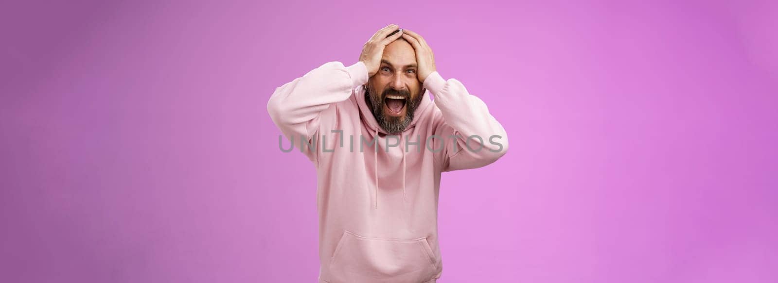Outraged furious mad adult man bearded yelling shocked despair hatefully looking camera insane holding hands head frowning shouting losing bet disappointed very upset standing purple background by Benzoix