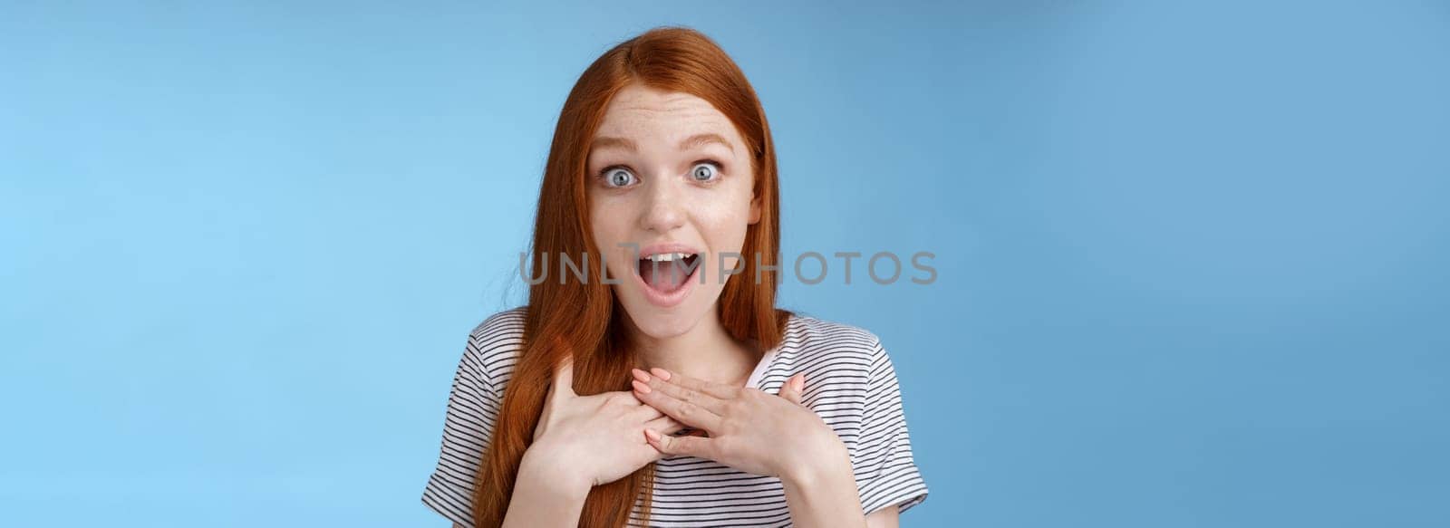 Amused happy grateful european redhead woman gasping drop jaw joyfully press palms chest thankful staring surprised incredible cool gift receive awesome proposal standing blue background by Benzoix