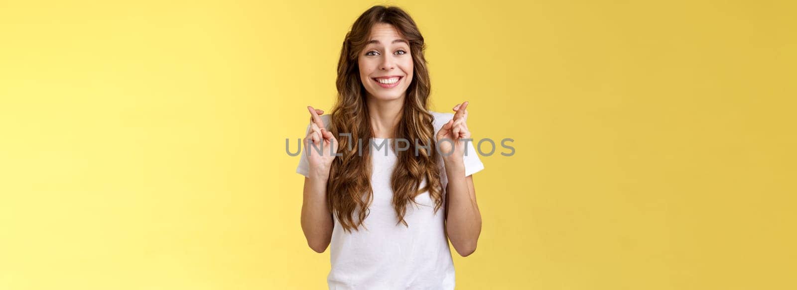Silly hopeful excited attractive caucasian girl curly haircut wishing optimistic smiling broadly cross fingers good luck anticipating miracle grinning excited implore praying fulfill desires by Benzoix