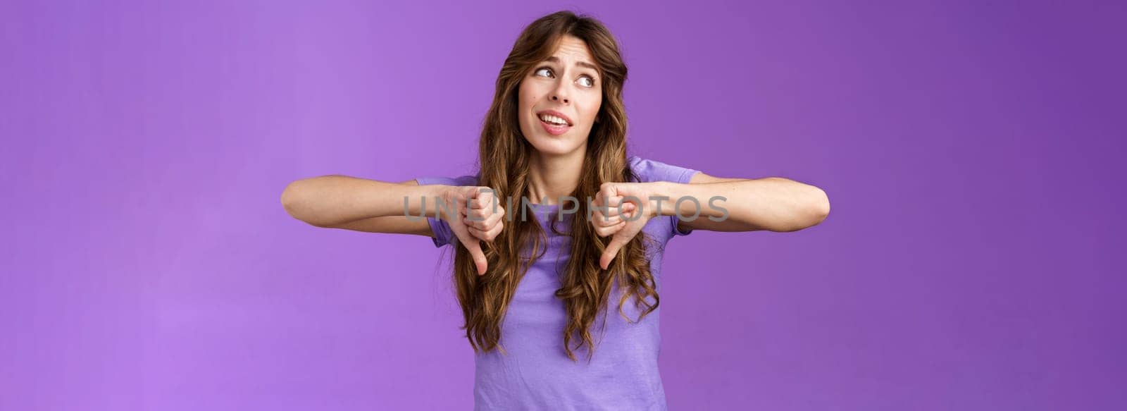 Unimpressed ignorant snobbish attractive curly-haired girl disagree lame idea look away disappointed show thumbs down dislike disapproval gesture not interested upset purple background by Benzoix