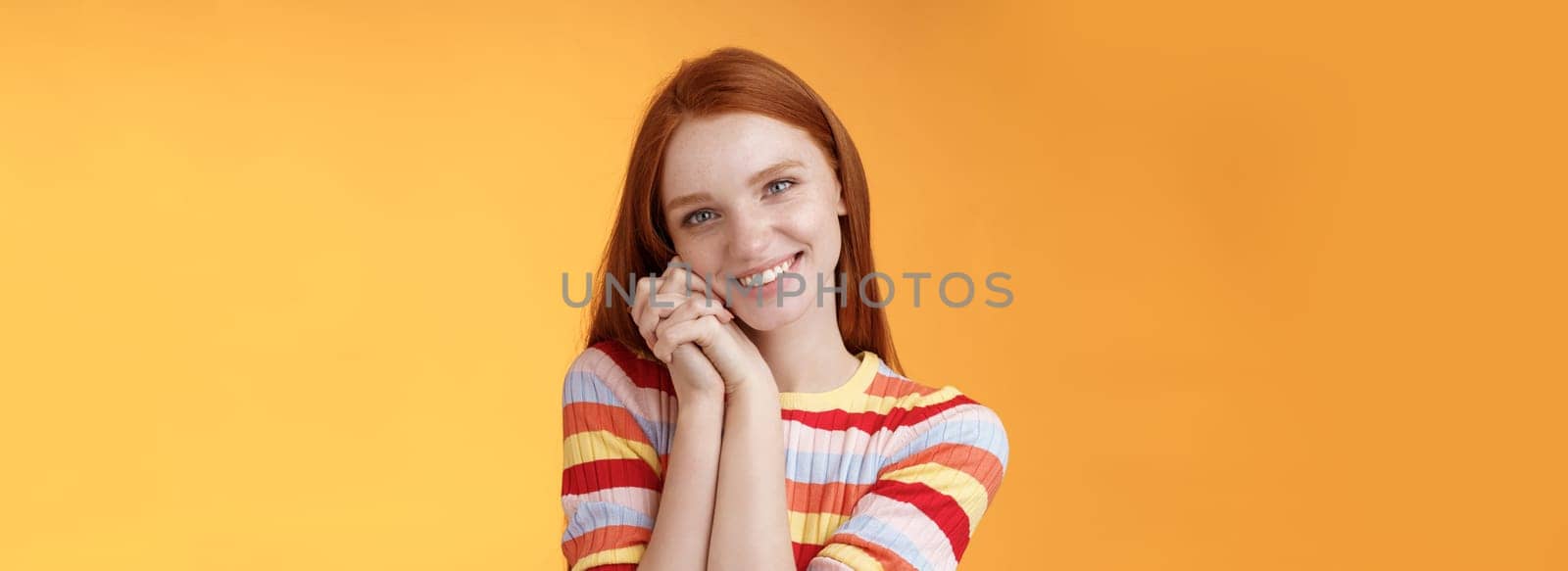 Romantic tender sensual attractive smiling redhead girlfriend melting heart feel warmth delighted lean palms grinning happily sweet gentle gift standing pleased orange background rejoicing thankful.