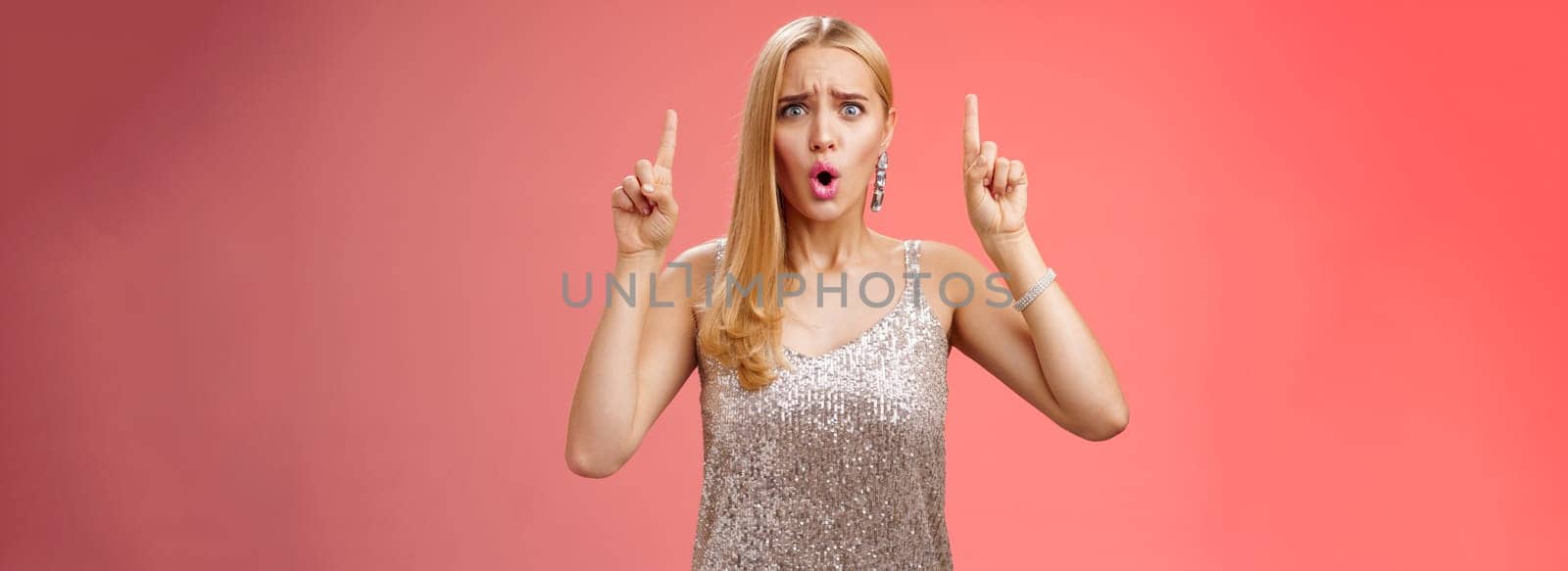 Upset gloomy complaining blond whining girl in silver stylish luxurious dress frowning cringing unhappy pointing up regret jealous tell boyfriend sale over, standing depressed sad red background.