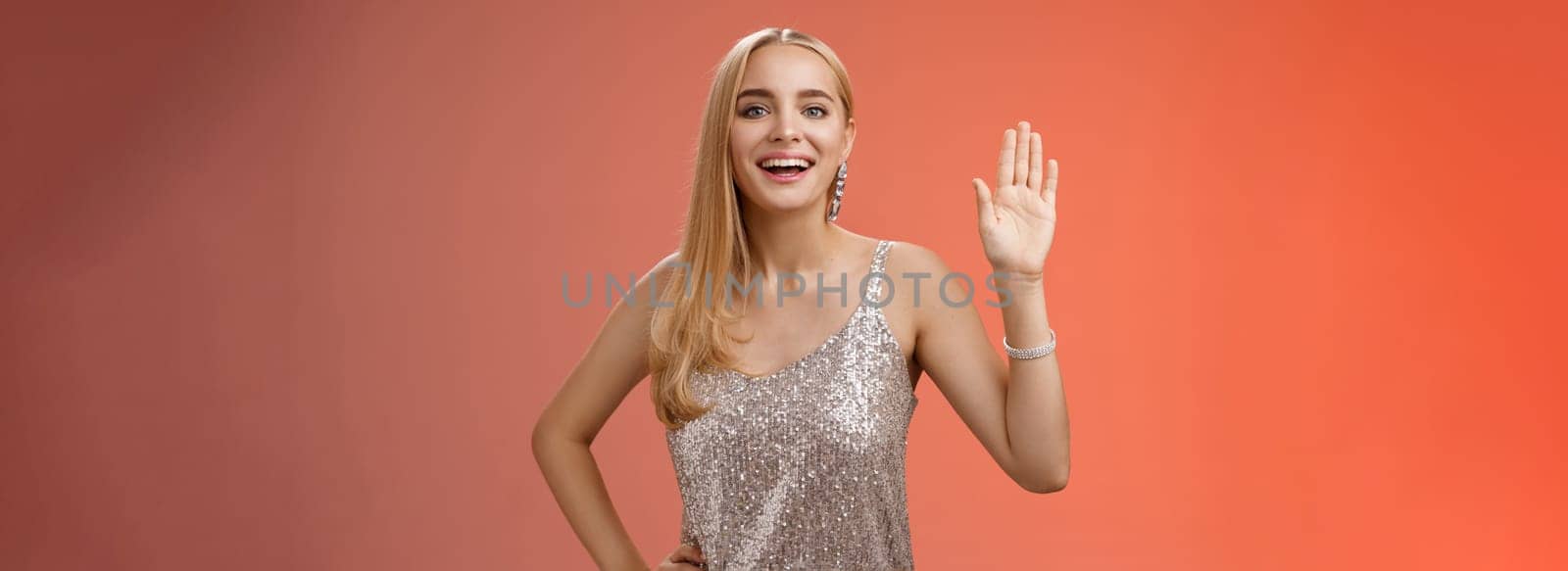 Friendly stylish glamour attractive blond caucasian woman in silver glittering dress hold hand waist waiving palm hello hi what up gesture smiling introducing herself party boyfriend friend by Benzoix