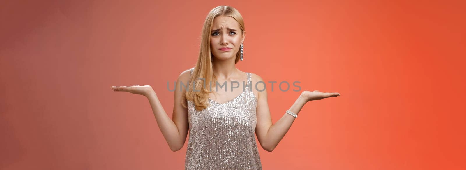Nervous unsure doubtful cute blond woman struggle make decision shrugging pointing sideways frowning upset standing insecure feel pressure cannot decide choice make, frustrated red background.