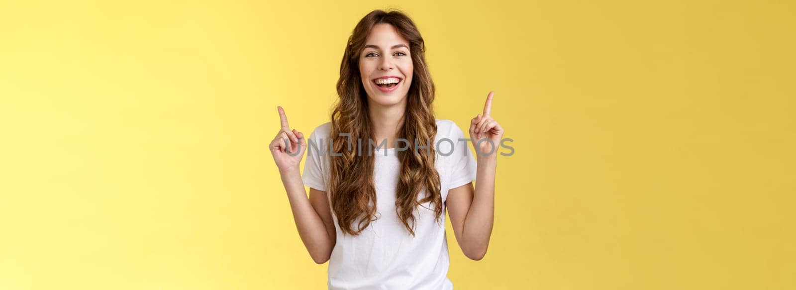 Charismatic enthusiastic attractive lively woman having fun enjoy awesome night out party laughing joyfully pointing up index fingers up introduce promo smiling happily yellow background by Benzoix