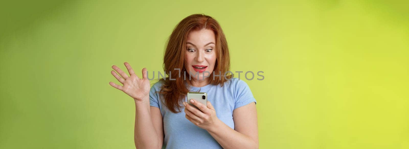 Surprised enthusiastic happy redhead mature middle-aged woman. receive excellent message read perfect news social media hold smartphone stare astonished pleased mobile phone screen raise hand triumph.