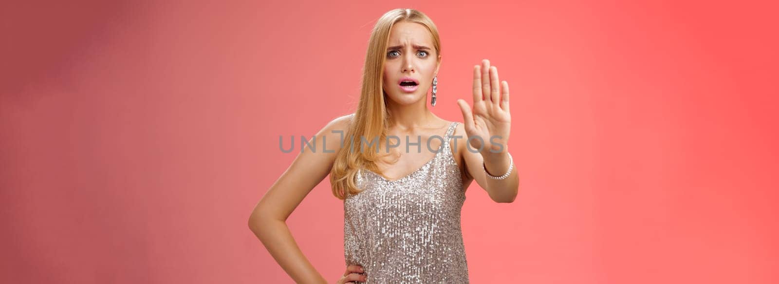 Freaked out displeased bothered insecure blond woman in silver glittering dress extend palm stop enough prohibition rejection gesture bothered pissed annoying clingy man nightclub, red background.