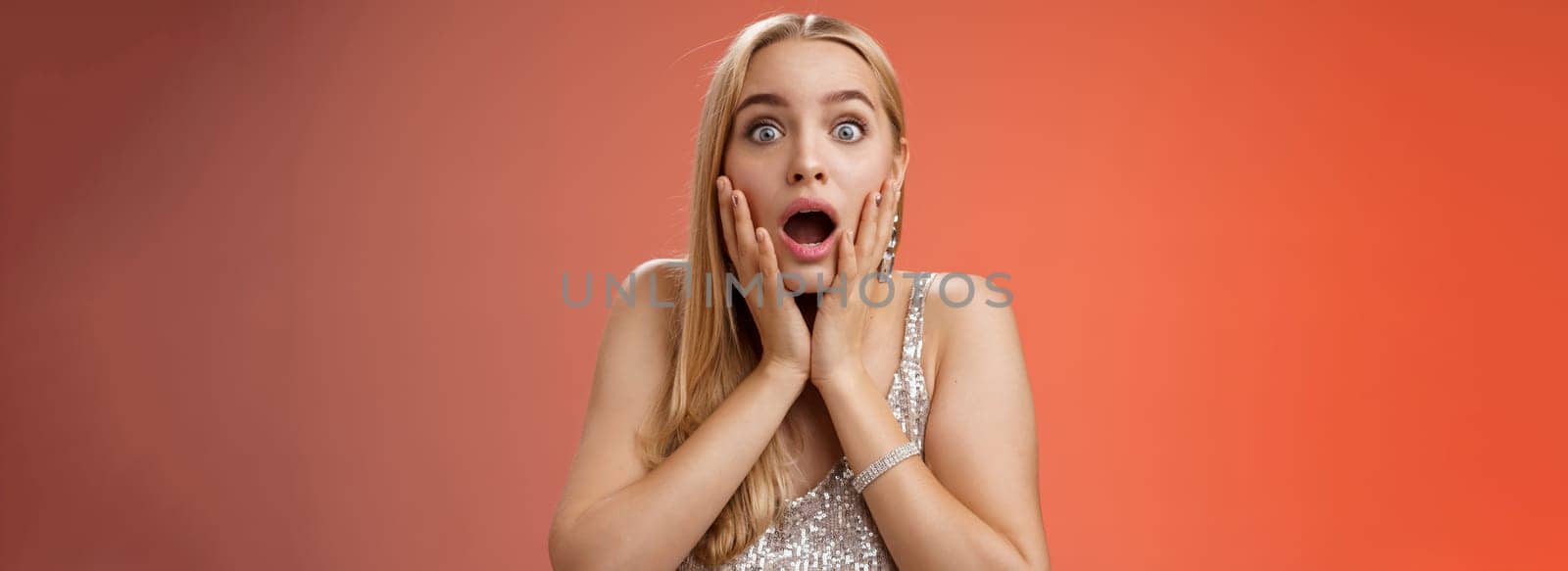 Shocked speechless concerned young stunned woman gasping screaming worried drop jaw touch cheeks widen eyes surprised nervously staring camera troubled afraid, standing red background.