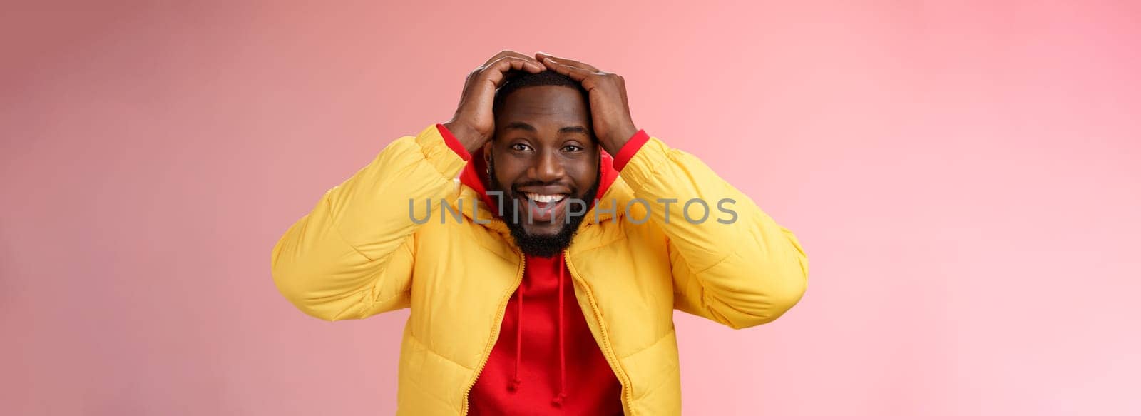 Waist-up surprised happy lucky young african-american bearded male in yellow jacket holding hands head smiling impressed joyfully receive awesome proposal dream come true, pink background by Benzoix