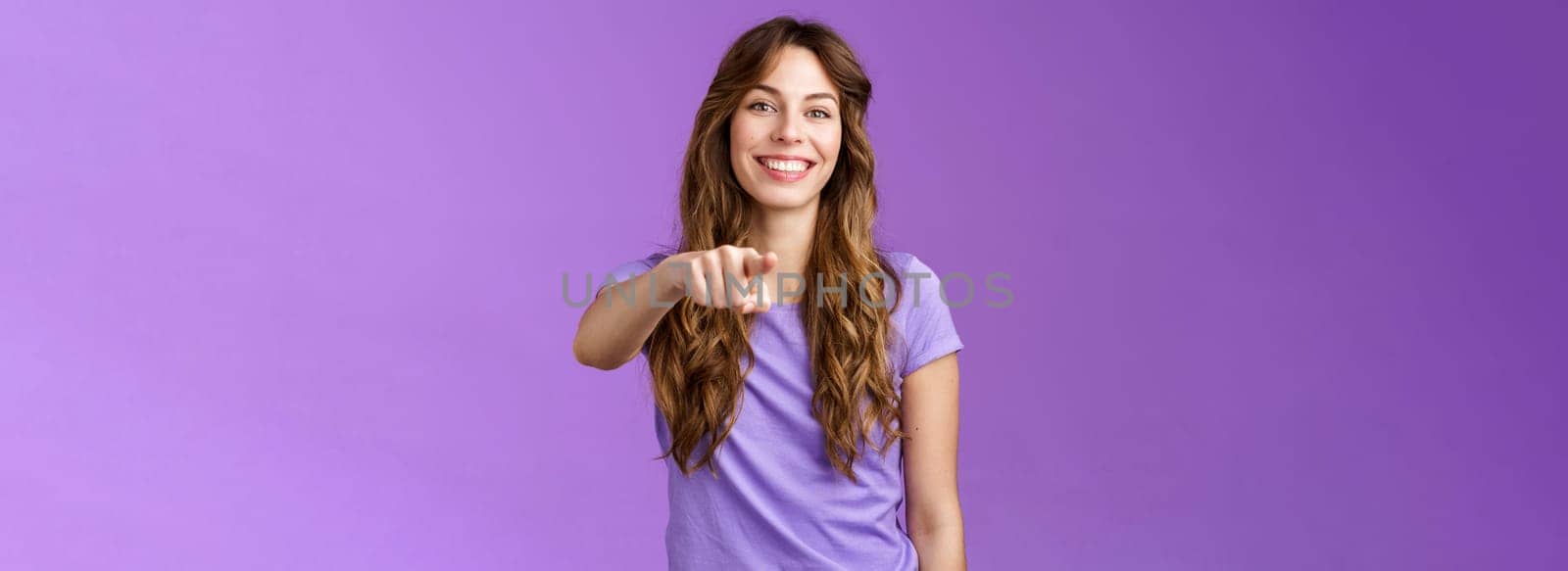 Cheerful girl pointing you. Attractive friendly happy smiling curly-haired female deciding who pick indicating finger camera grinning joyful inviting coworker her team stand purple background by Benzoix